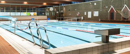 Bassängen i Kärra simhall sedd från ett hörn. I förgrunden syns en plint och handtag till trappan ner i bassängen. Vattnet är stilla.