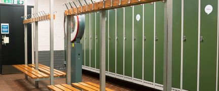 Omklädningsrum i Kärra simhall. Skåpen har mörkgröna metalldörrar. I mitten av rummet finns träbänkar med krokar ovanpå.