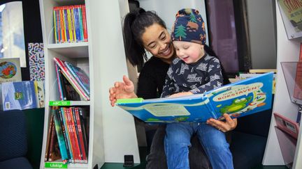  En vuxen med ett litet barn i sitt knä bläddrar i en stor bilderbok. Foto: Lo Birgersson