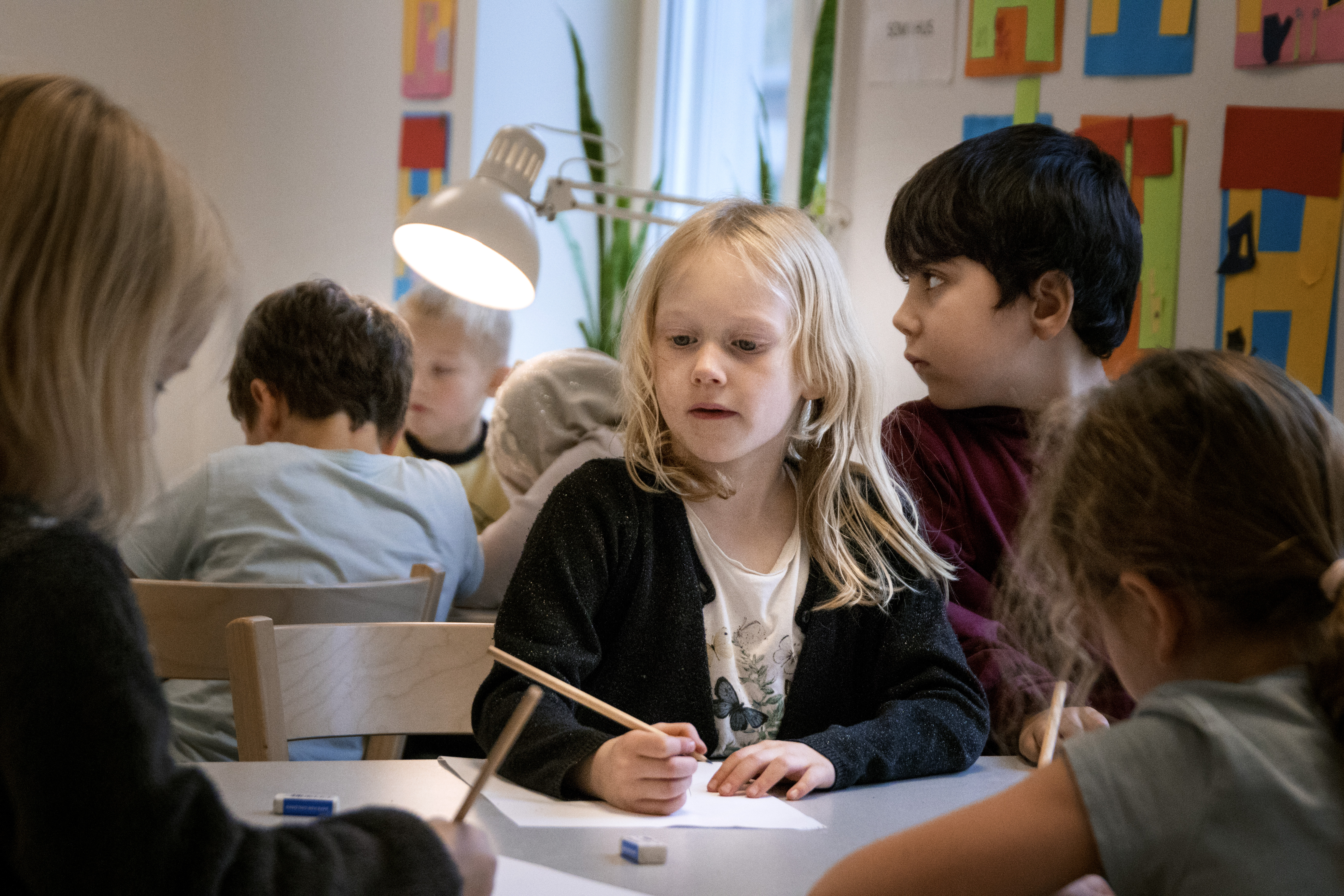 Elever i förskoleklass som sitter vid bordet med penna och papper.