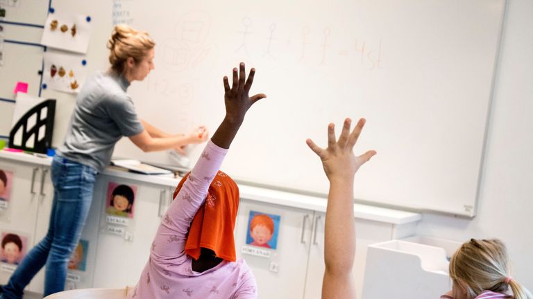 Barn räcker upp handen framför lärare. 