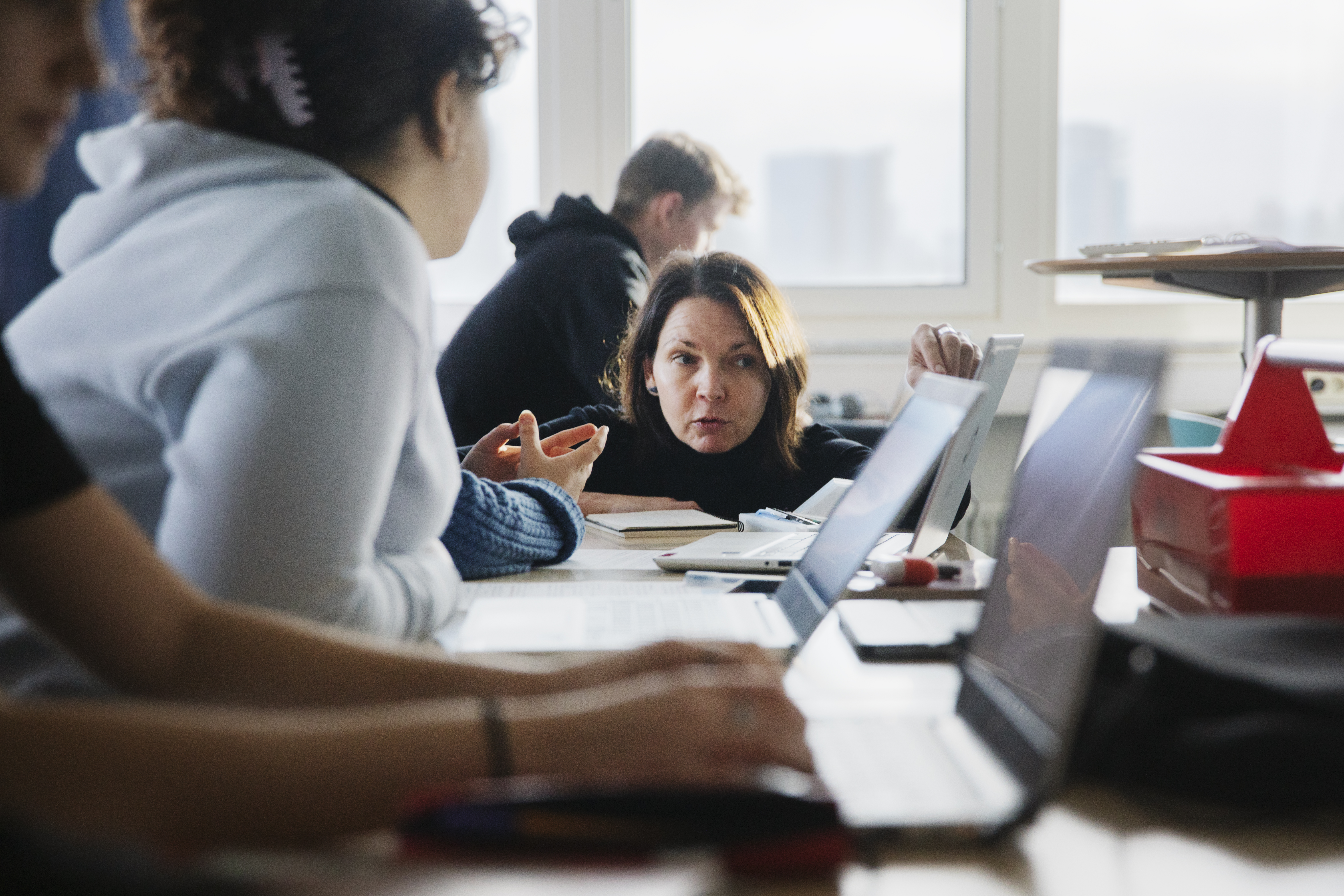 Ett foto av elever som sitter i ett klassrum och en lärare som hjälper till.