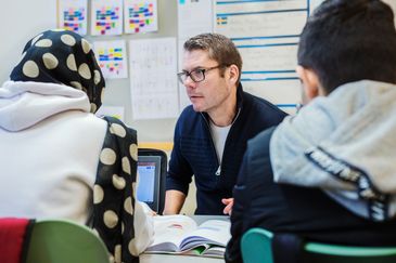 Två elever pratar med en lärare som sitter mitt emot dem i klassrummet.