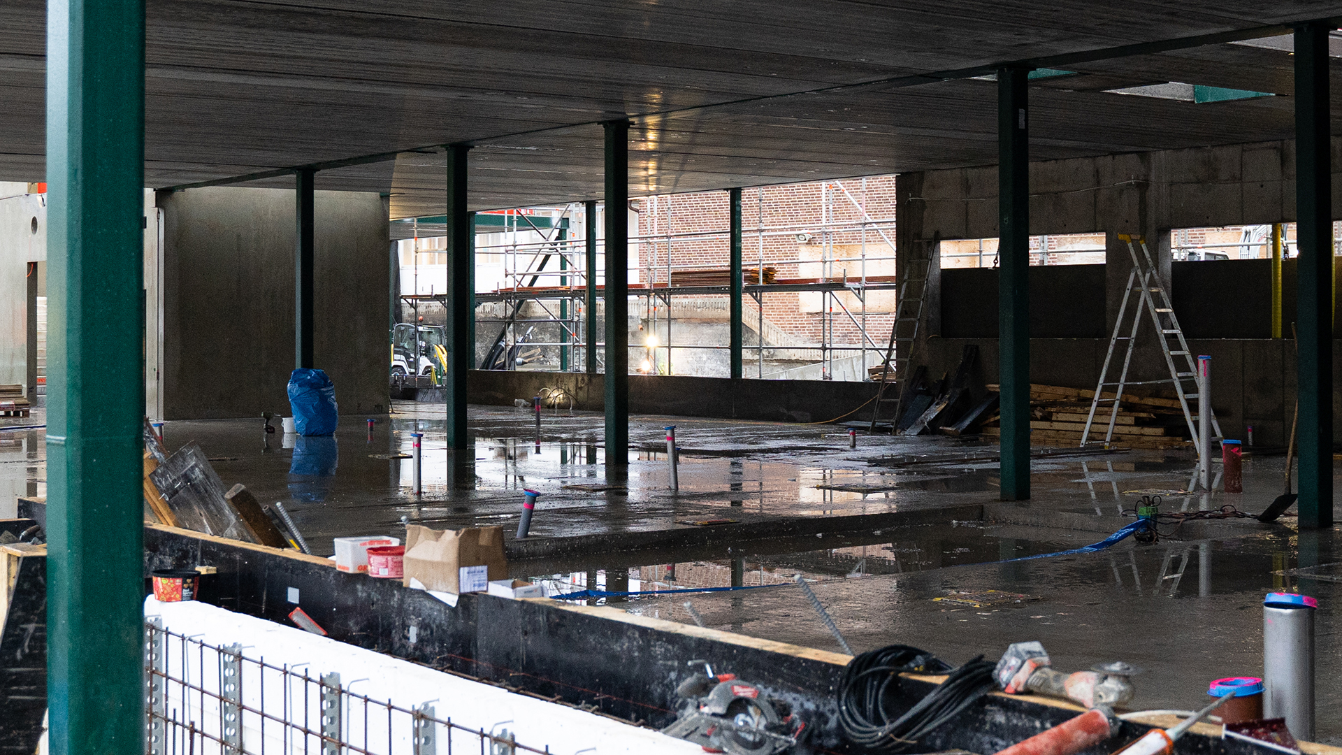 Ett regnvått betonggolv och ett betongtak som hålls uppe av gröna stålbjälkar.