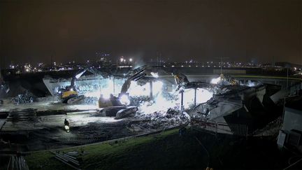 Nattlig arbetsplats där flera stora grävmaskiner river en betongbro.