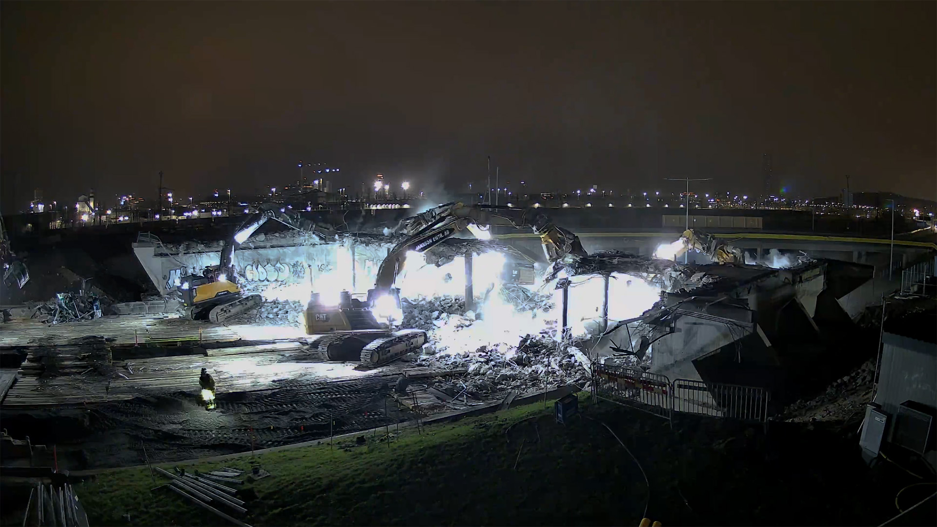 Nattlig arbetsplats där flera stora grävmaskiner river en betongbro.