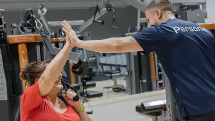 En ung man ur personalen ger en äldre kvinnlig besökare som använder en styrkemaskin en high five.