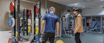 En person med personaltröja pratar med en besökare på gymmet.