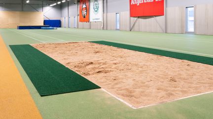 Friidrottshallen i Angered Arena. I förgrunden syns en yta fylld av sand, omgiven av gröna mattor.