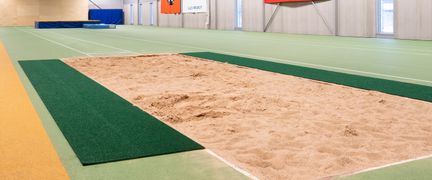 Friidrottshallen i Angered Arena. I förgrunden syns en yta fylld av sand, omgiven av gröna mattor.