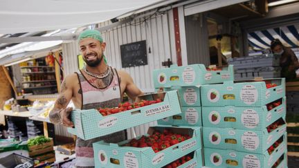 Person lyfter stora lådor med jordbubbar i marknadsmiljö