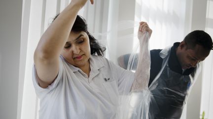 Två personer inom vården tar på sig plastförkläden.