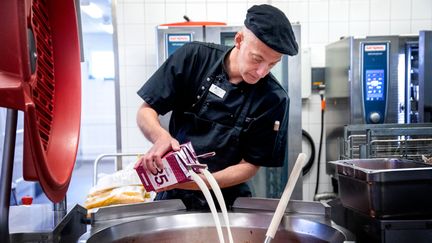 Kock häller mjölk i en stor kastrull.