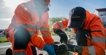 Två gatuarbetare genomför ett arbete i utomhusmiljö.
