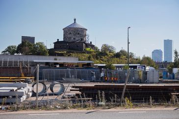 Inhägnat område med byggmaterial. I bakgrunden syns höghus och stadsmiljö.