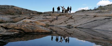 Några personer står på ett berg och deras spegelbilder syns i vattnet nedanför.
