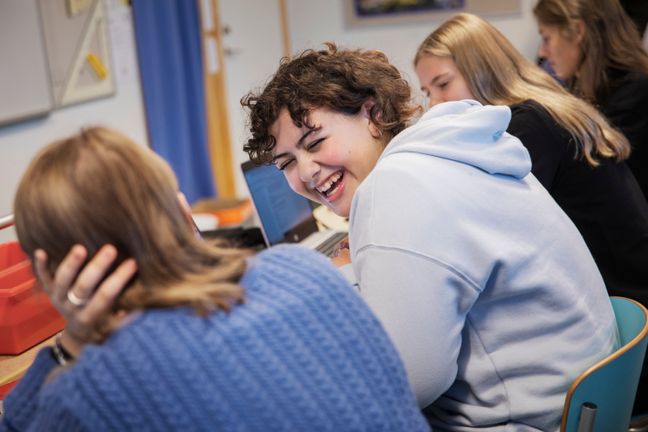 Glada elever som skrattar och sitter i första bänkraden i ett klassrum.