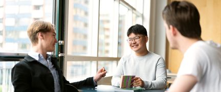 Tre elever sitter vid ett bord och pratar och skrattar. 