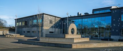En skulptur med sittplatser på Glöstorpsskolans skolgård med ett pingisbord i bakgrunden.