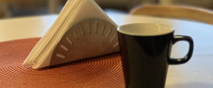 En kaffemugg och ett ställ med servetter står på ett bord.