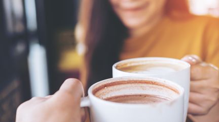 Två personer skålar med kaffemuggar.