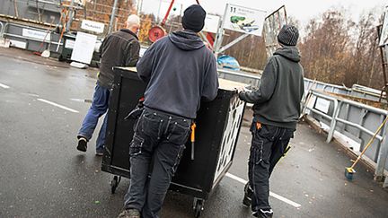 Tre personer går med en vagn på återvinningscentral.