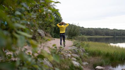 En man joggar på en stig med en skog i bakgrunden.