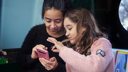 En vuxen och ett barn använder en mobiltelefon tillsammans.