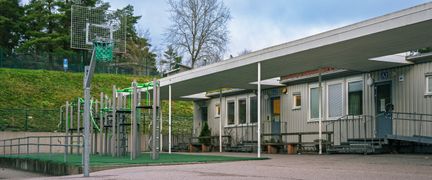 En skolgård med en klätterställning framför skolbyggnaden.