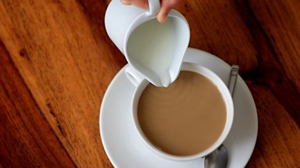 En person häller mjölk i en kaffekopp.