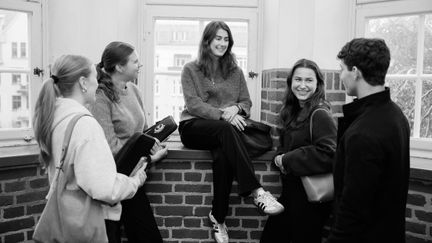 En grupp elever som står och sitter framför ett fönsterparti i korridoren