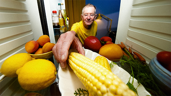 Man i gul t-shirt tar ut en majskolv från sitt kylskåp