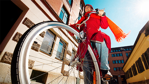 Kvinna på cykel i röd kappa och halsduk 