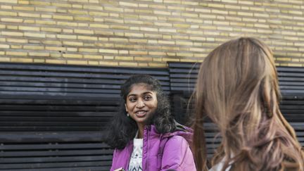 Två ungdomar går utomhus och pratar och ler mot varandra.