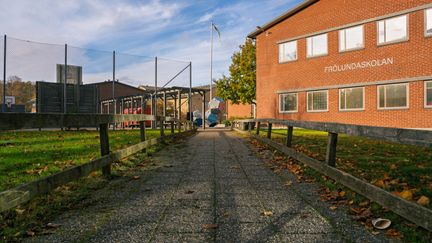 En tegelbyggnad med texten Frölundaskolan på fasaden som ligger bredvid en skolgård