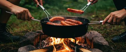 Två personer grillar korv över en eld.