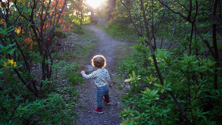Litet barn går på en stig i grönska och solnedgång.