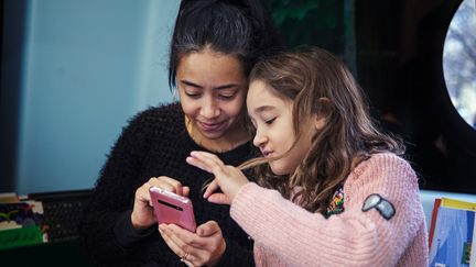 En vuxen och ett barn tittar i en mobiltelefon.