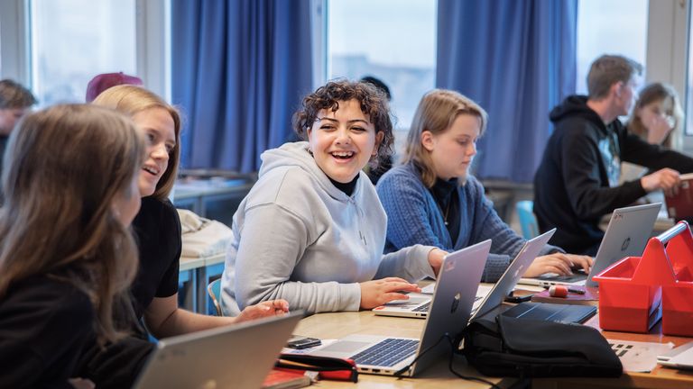 Bild på flera glada elever som sitter vid sina datorer i skolan.