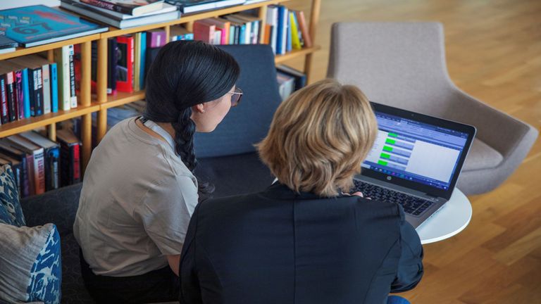 Två personer sitter på ett kontor och läser på en dator.