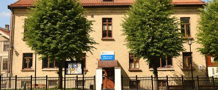 en gul tegelbyggnad med en röd dörr och röda fönster. Framför huset finns två träd.