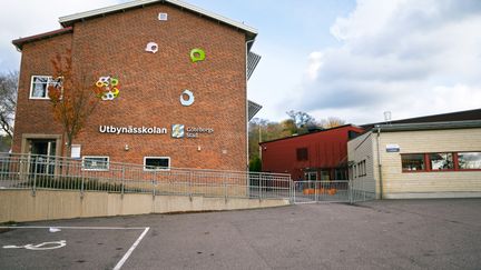 En skolbyggnad i tegel med en parkeringsplats framför