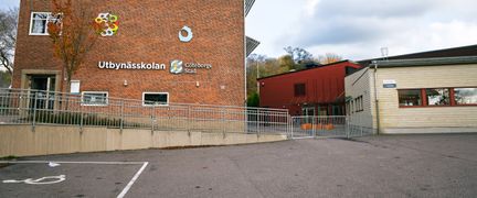 En skolbyggnad i tegel med en parkeringsplats framför