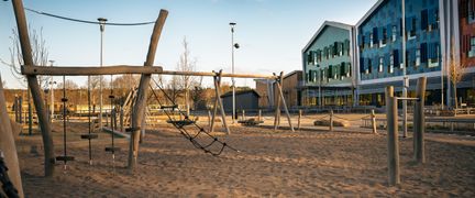 En tom skolgård med klätterställningar i sandlådan och några skolbyggnader i bakgrunden.