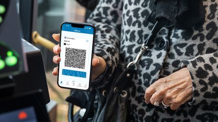 Närbild på en persons händer som håller upp en mobiltelefon där man ser mobilbiljetten.