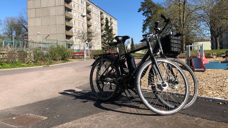 Två cyklar står parkerade bredvid varandra, med cykelbana i bakgrunden.