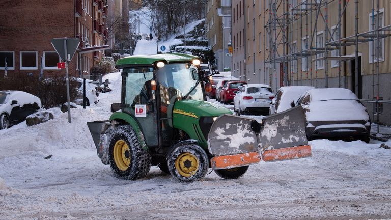 En grön traktor med plog plogar en snötäckt Torkelsgata.
