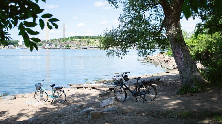 Två cyklar står parkerade på en liten sandstrand omgiven av träd.