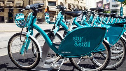 Flera blå cyklar med texten Styr & Ställ står parkerade på rad.
