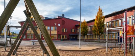En skolgård med gungor framför en röd skolbyggnad.